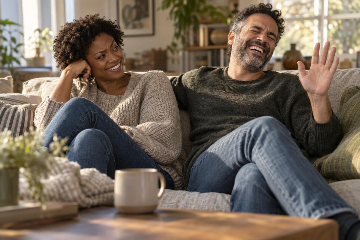 Couple on a sofa laughing together, woman raising an eyebrow in playful disbelief