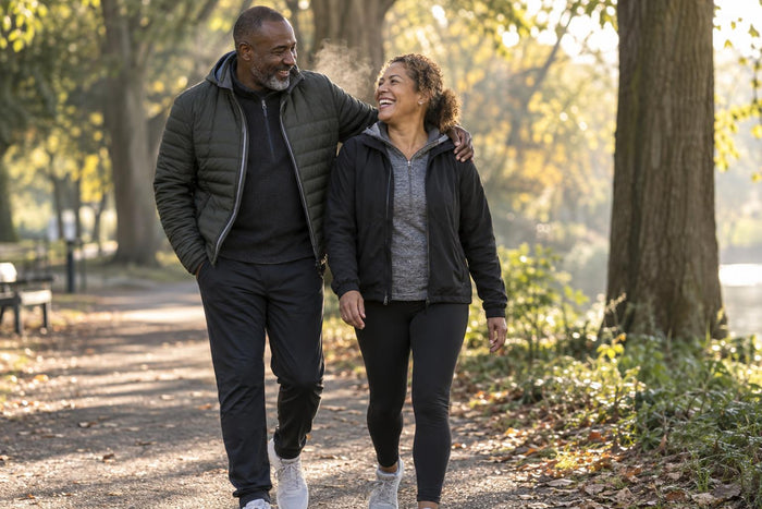 Couple in their late forties walking and laughing together on a sunlit park path